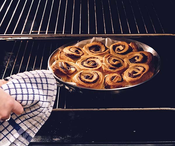 Person taking cinnamon rolls out of the oven