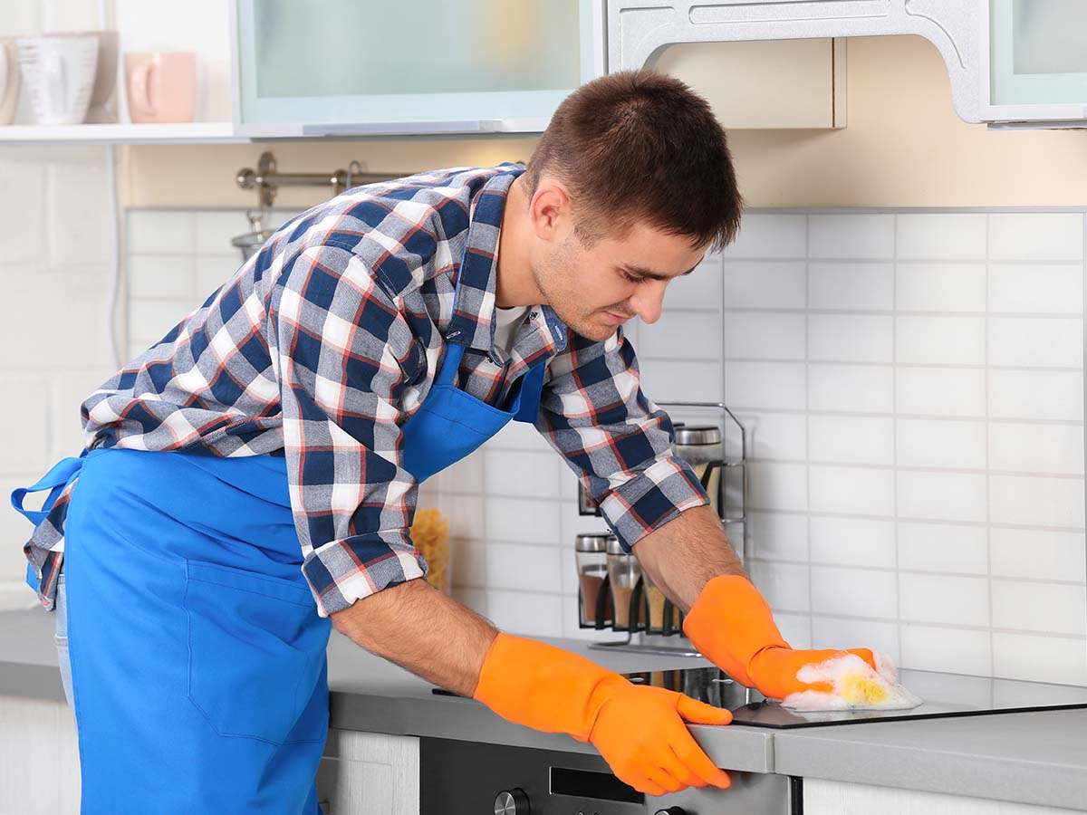 Image of a man wearing an apron and gloves while cleaning the kitchen