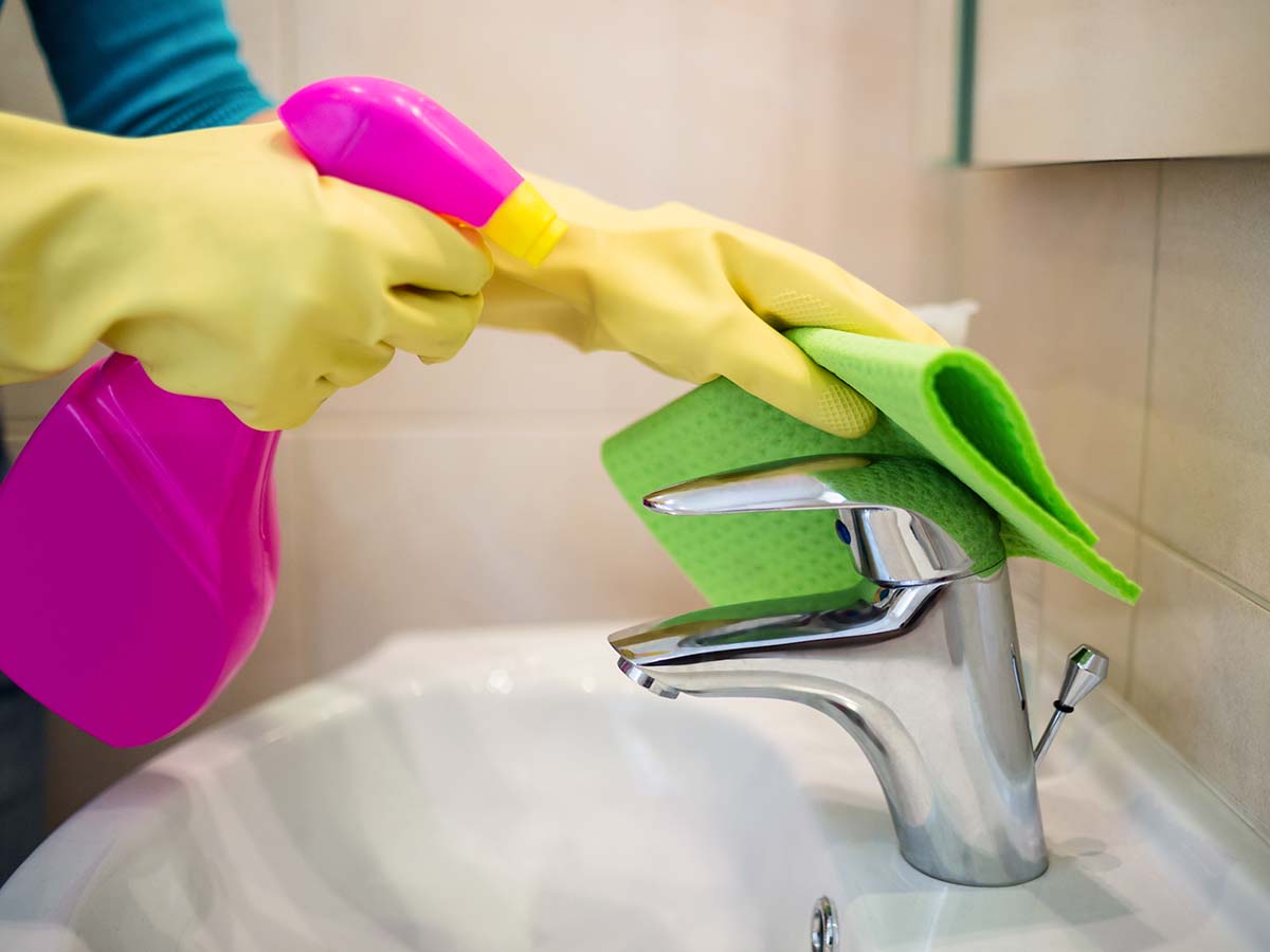 Image of someone wearing gloves and cleaning the bathroom faucet