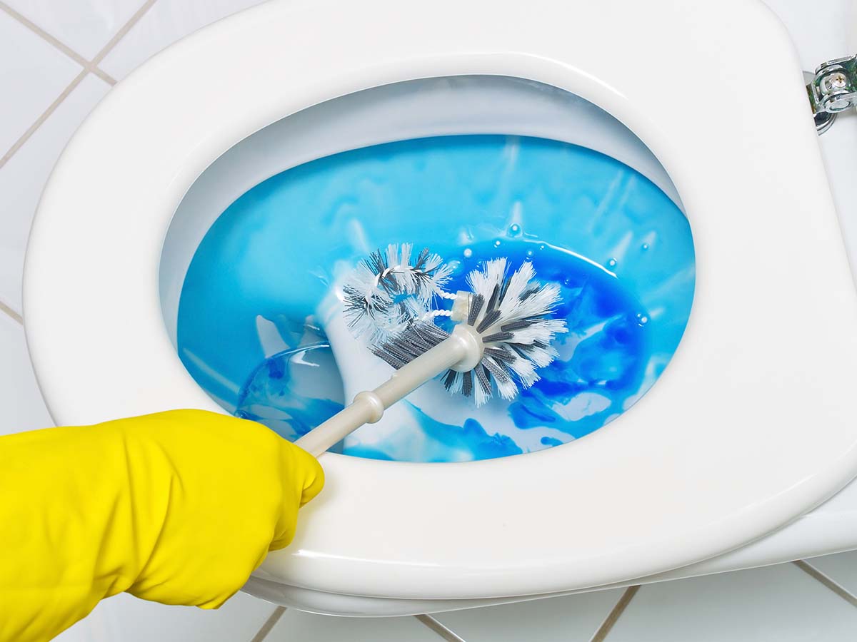 Image of someone wearing yellow gloves and cleaning the toilet with a brush