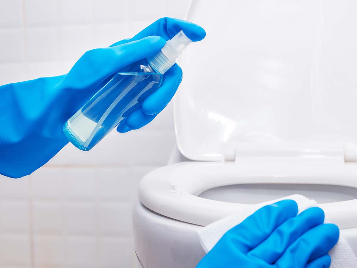 Image of someone earring blue gloves and cleaning the toilet