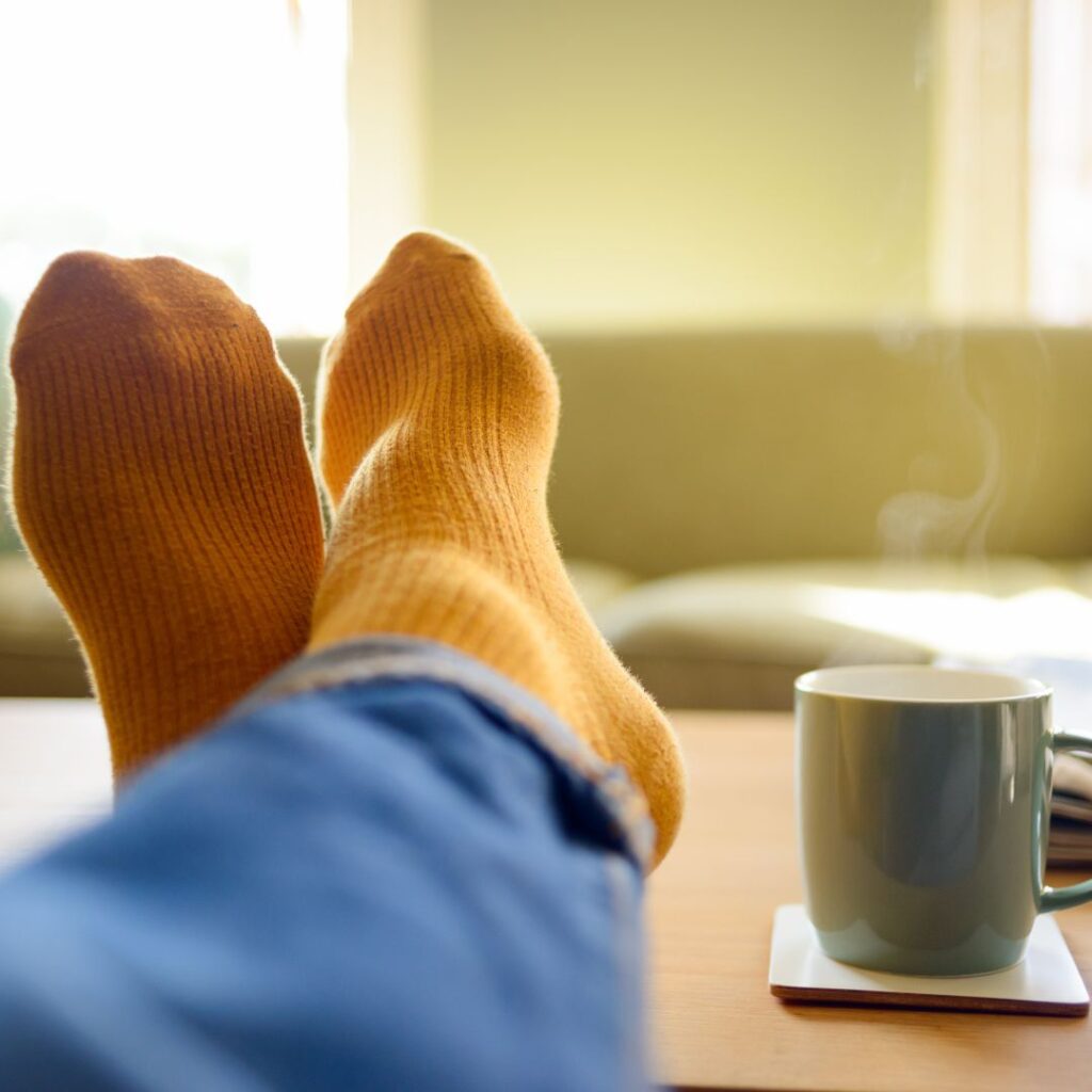 An image of feet on a table next to a cup of coffee.